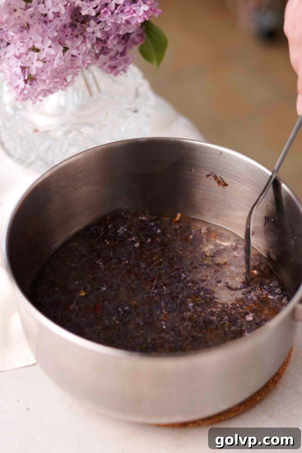 stirring cooked lilac syrup in a saucepan with a spoon