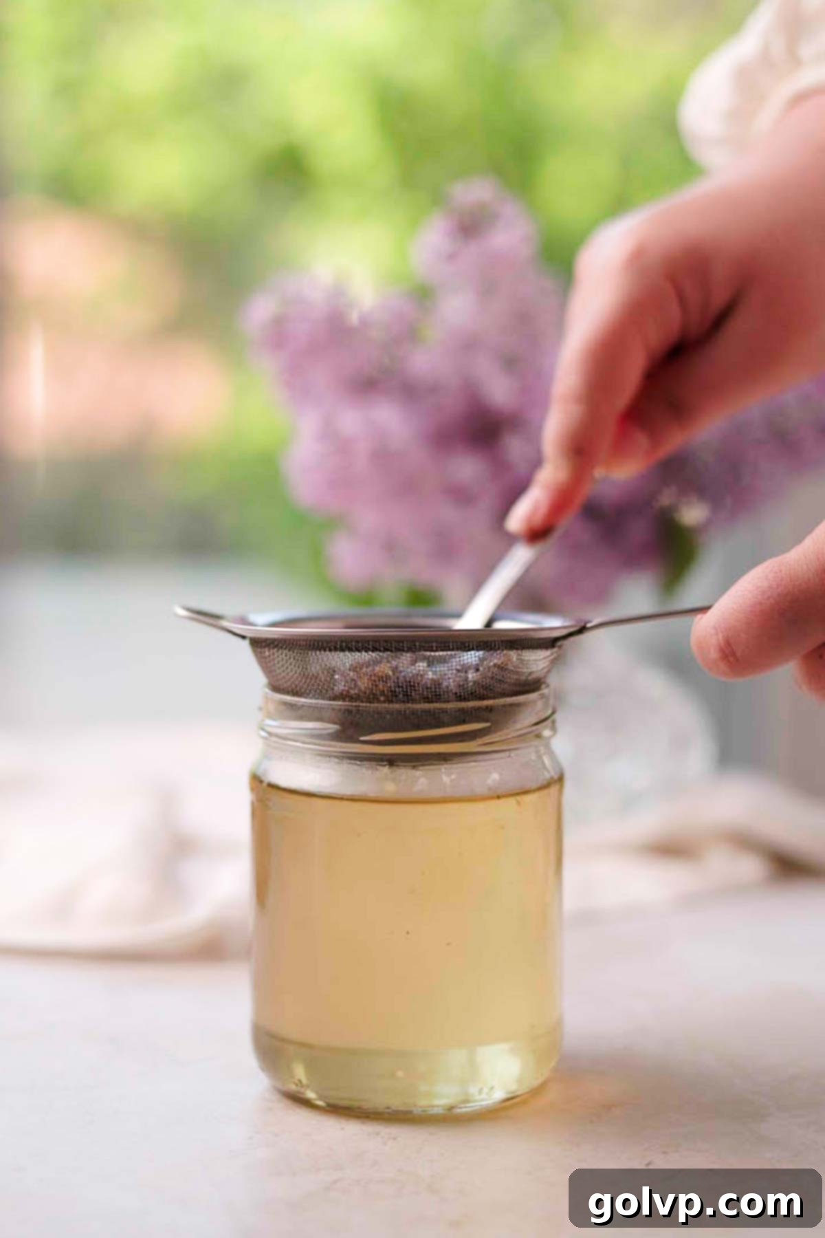 straining lilac syrup through a metal sieve into a glass jar