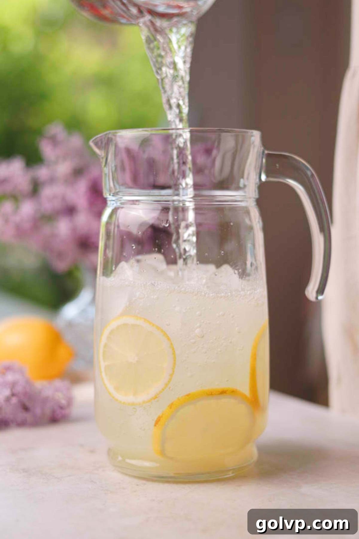 pouring water into a glass pitcher with lemon juice and ice