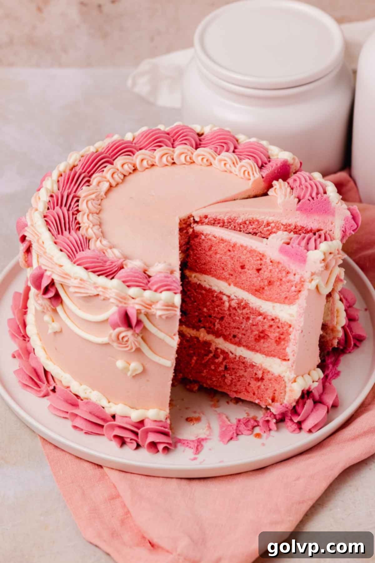 pink velvet cake with elaborate piped decorations and a few slices taken out of it