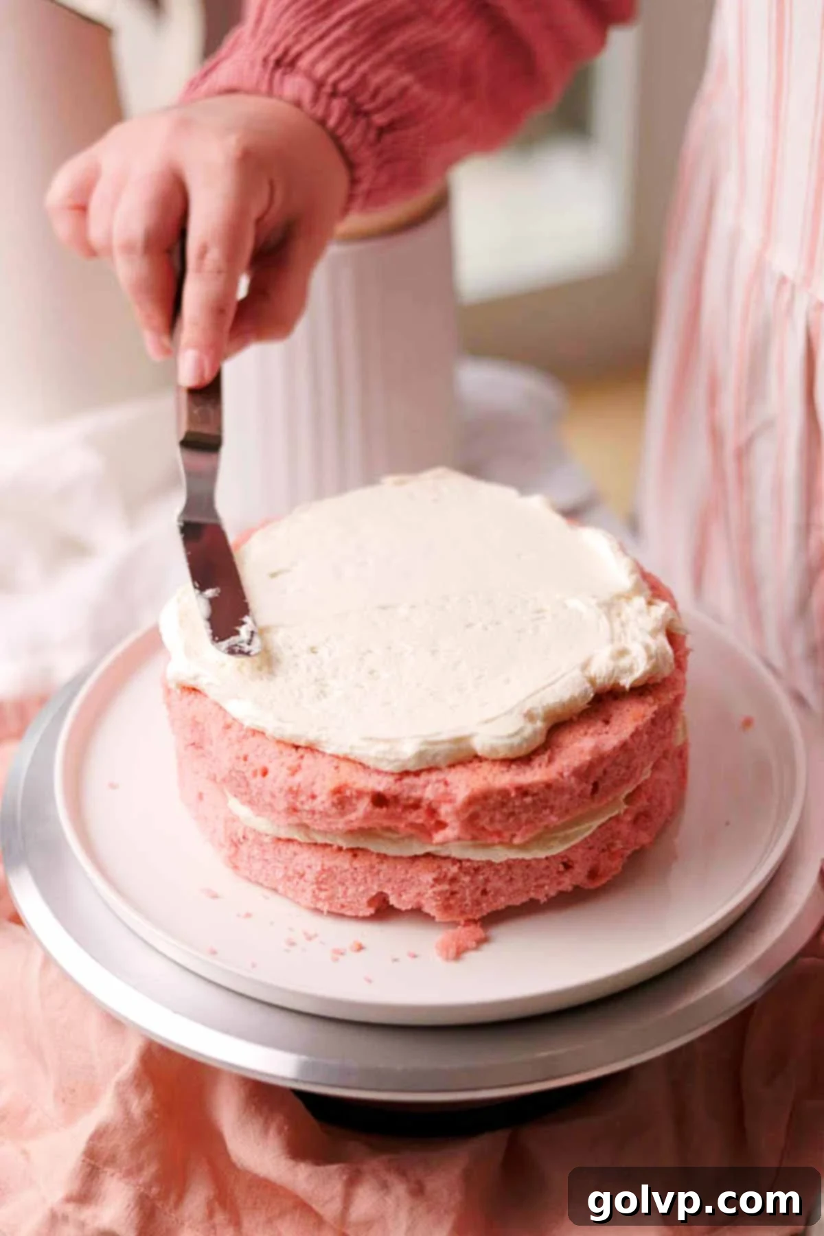frosting pink cake layers with white frosting using a small offset spatula