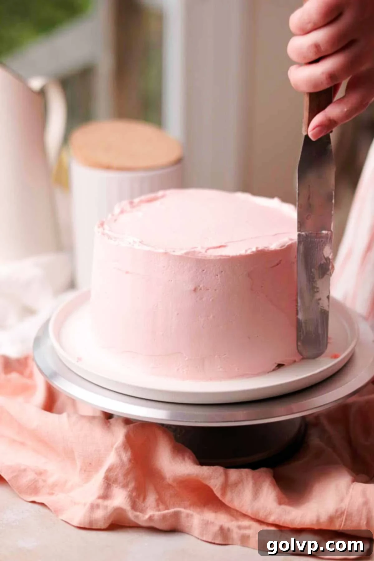Using long metal spatula to frost cake with pink cream cheese frosting