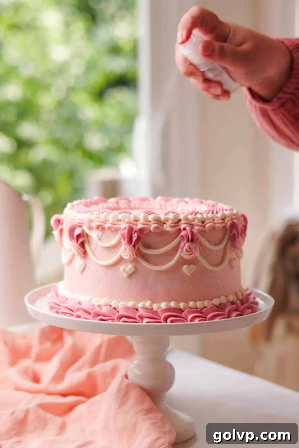 spraying top of decorated vintage pink velvet cake with edible glitter
