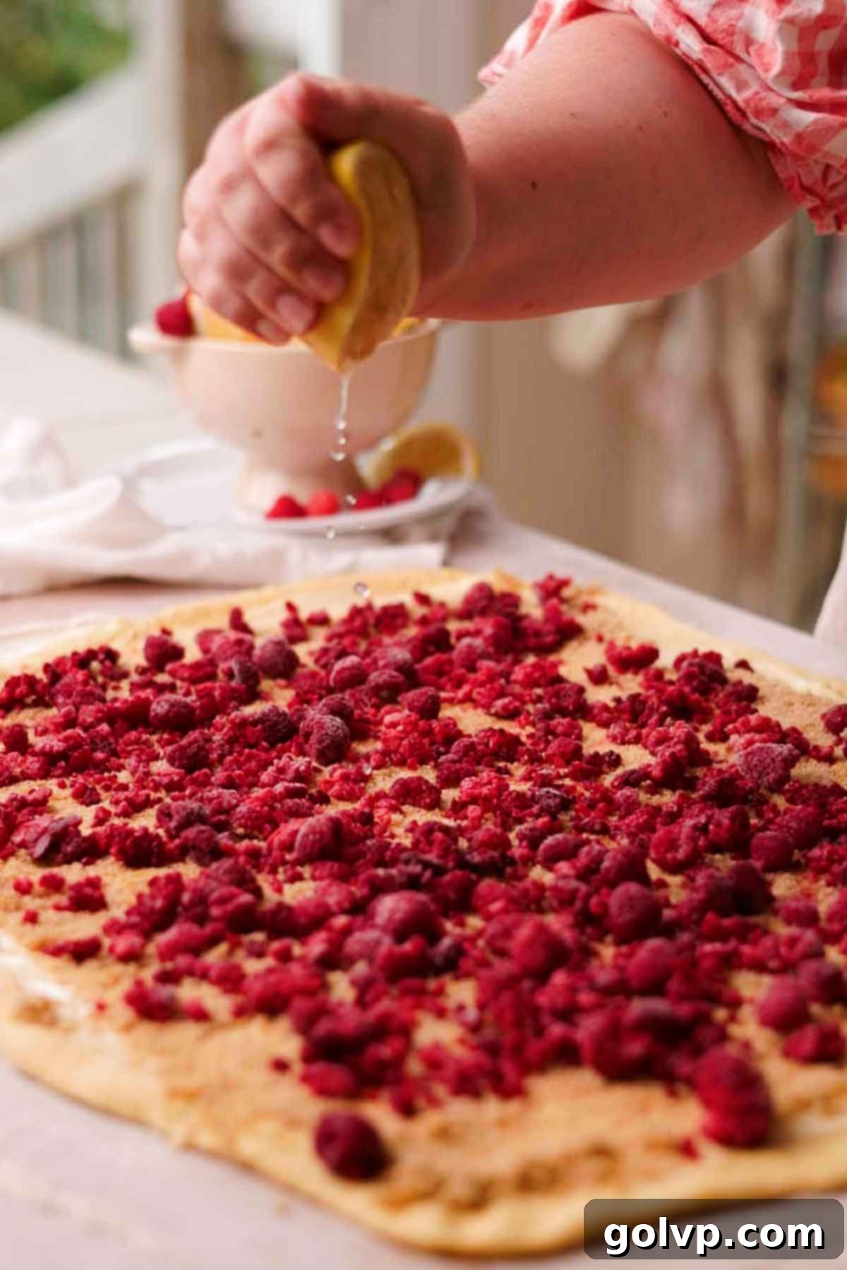 drizzling lemon juice over raspberry covered dough