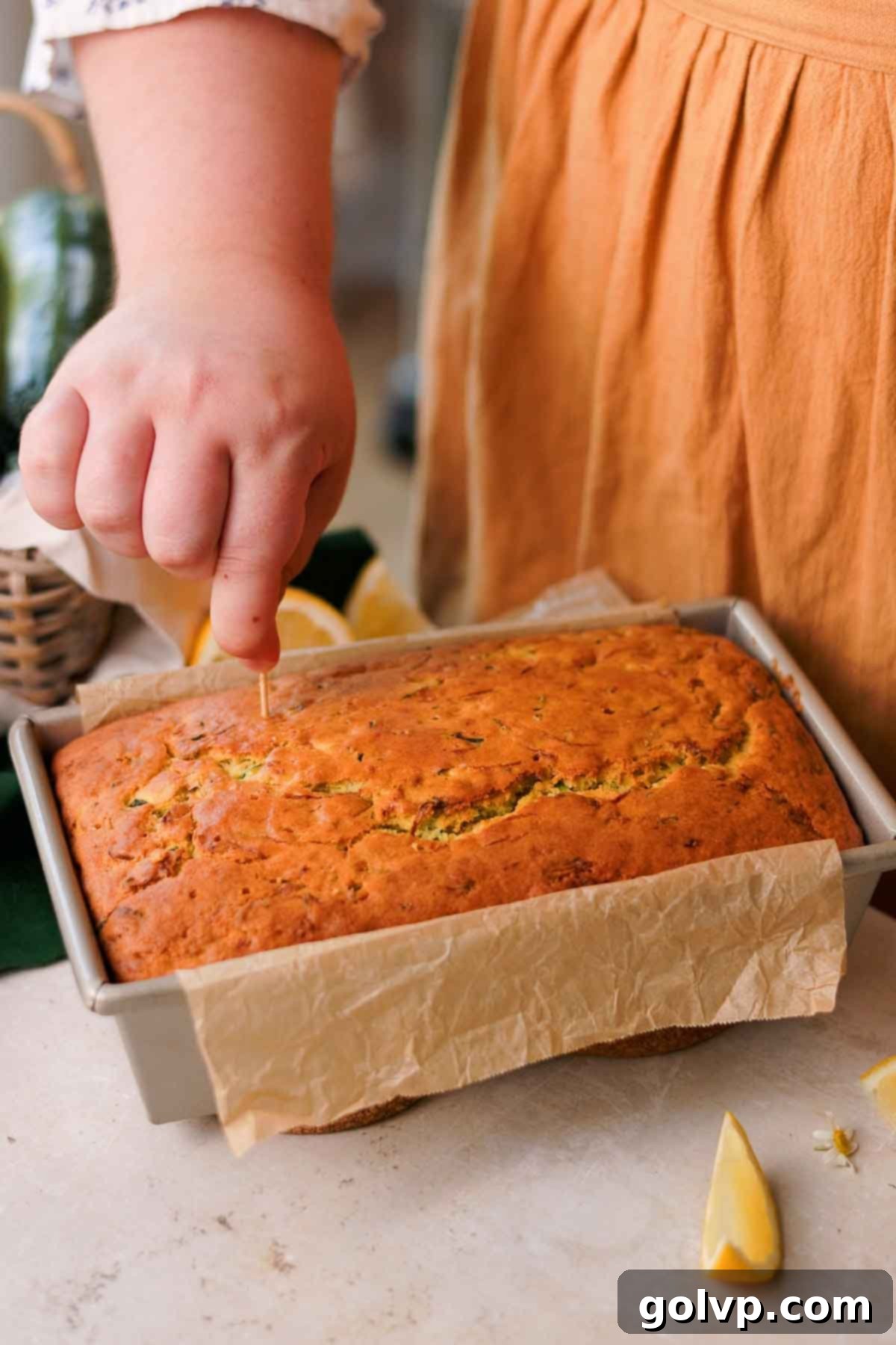 A toothpick being inserted into the top of a freshly baked lemon zucchini loaf to check for doneness and prepare for the drizzle.