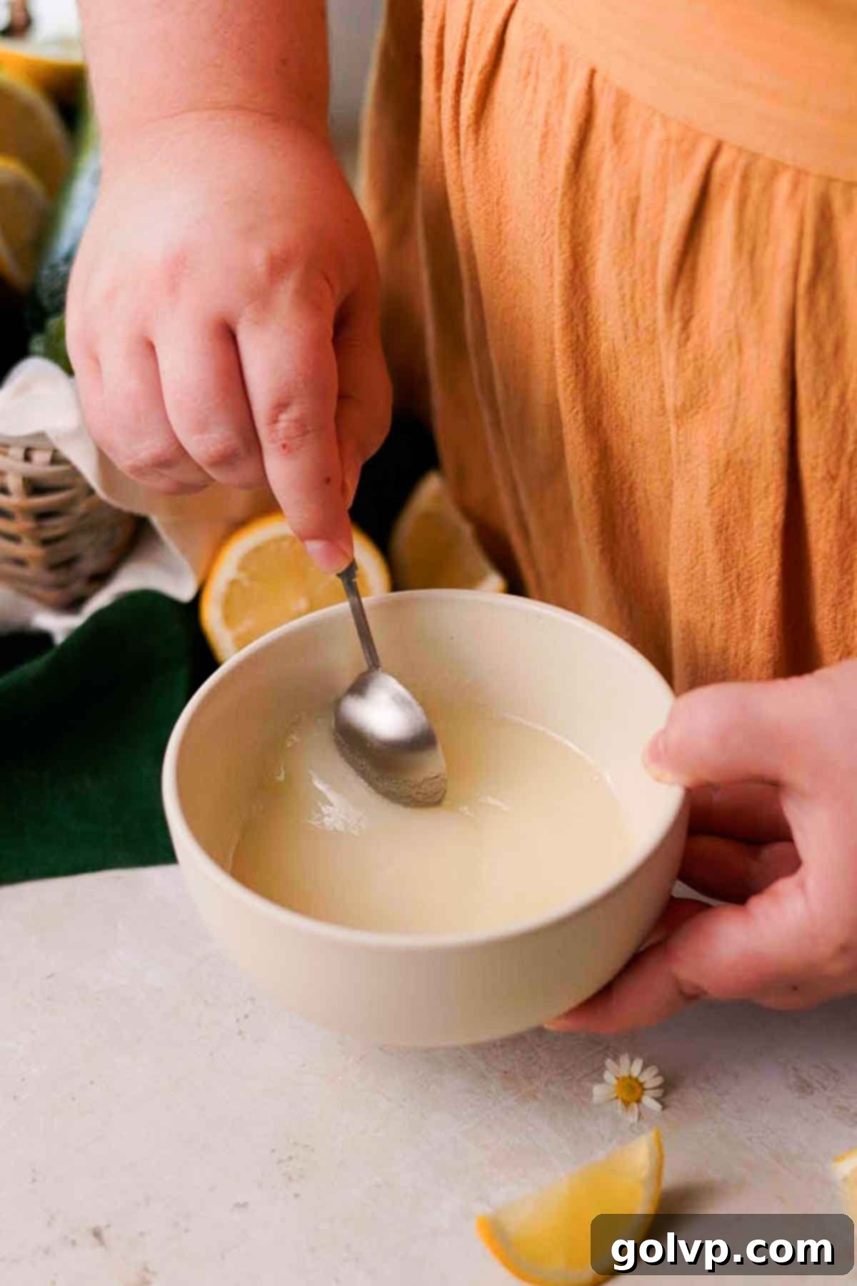 A small bowl containing lemon juice and granulated sugar, being stirred with a spoon to create the lemon drizzle.