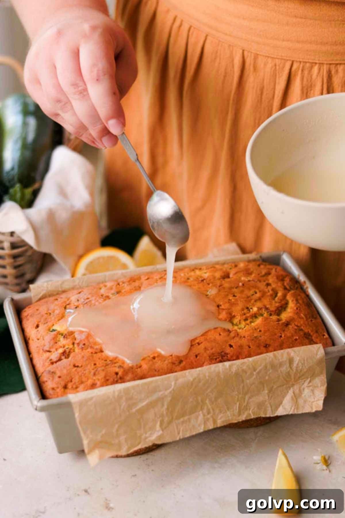 Lemon drizzle being poured evenly over the hot lemon zucchini loaf, allowing it to soak into the poked holes.
