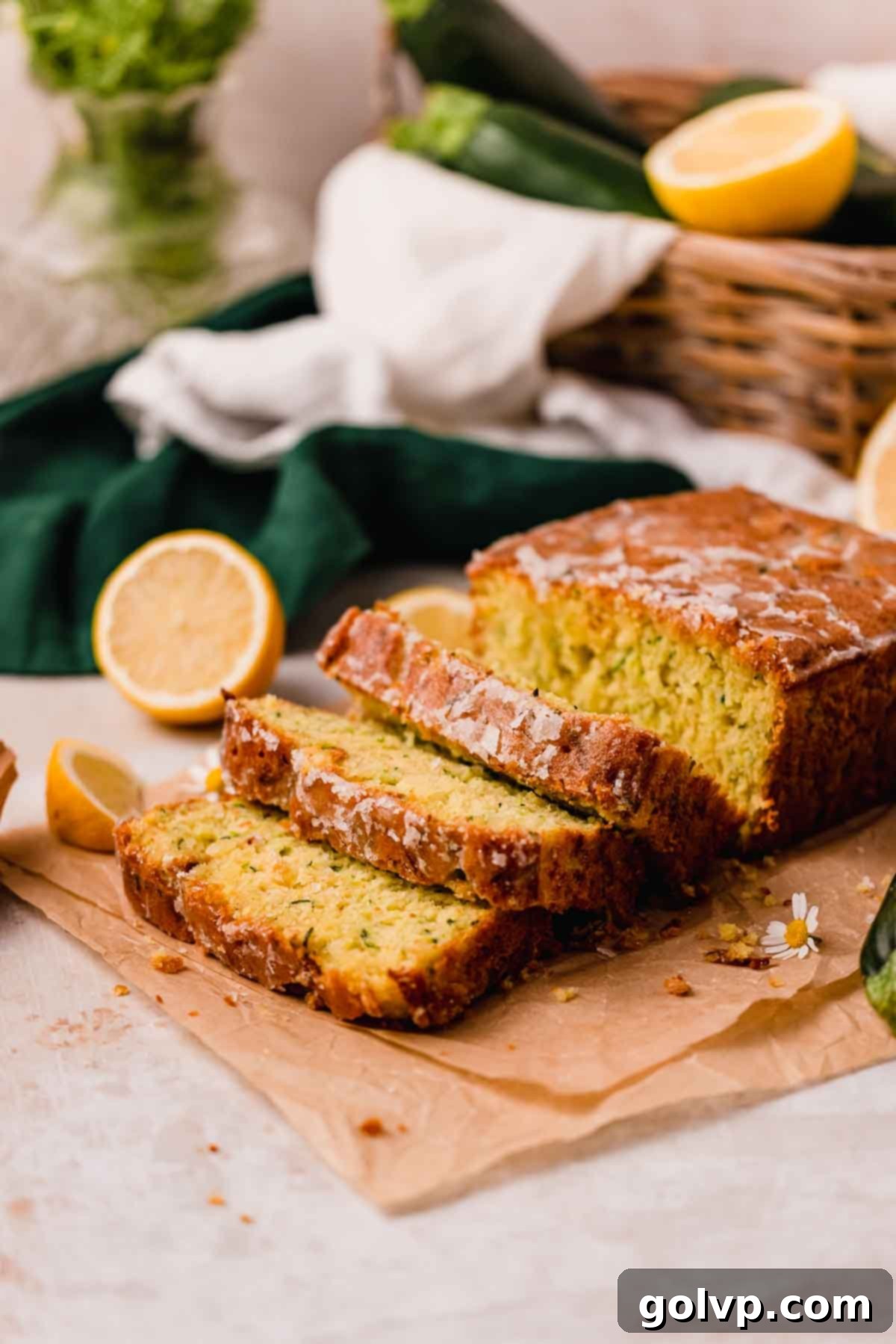 A perfectly sliced loaf of lemon zucchini bread with fresh green zucchini in the background, highlighting the fresh ingredients.