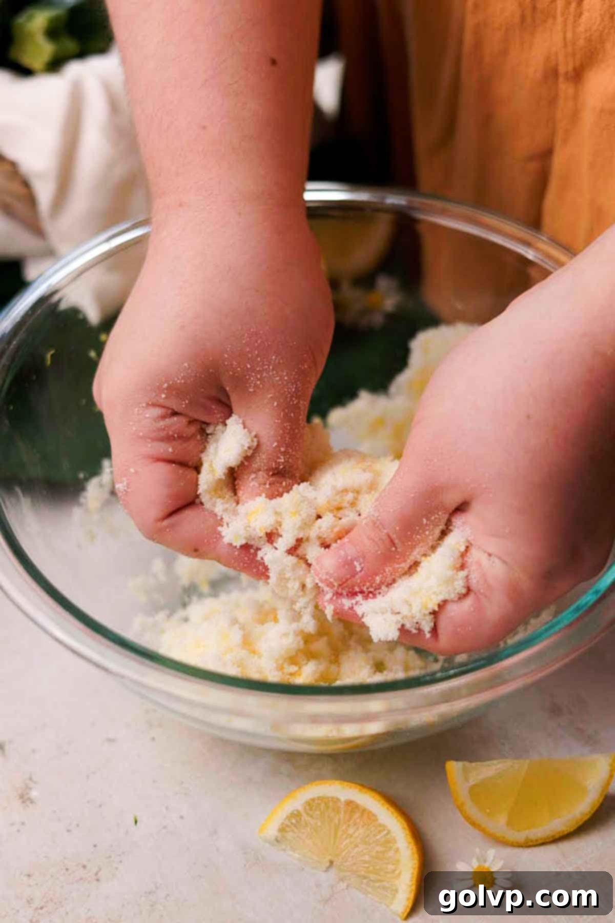 Hands rubbing lemon zest and granulated sugar together in a large bowl, releasing a fragrant citrus aroma.