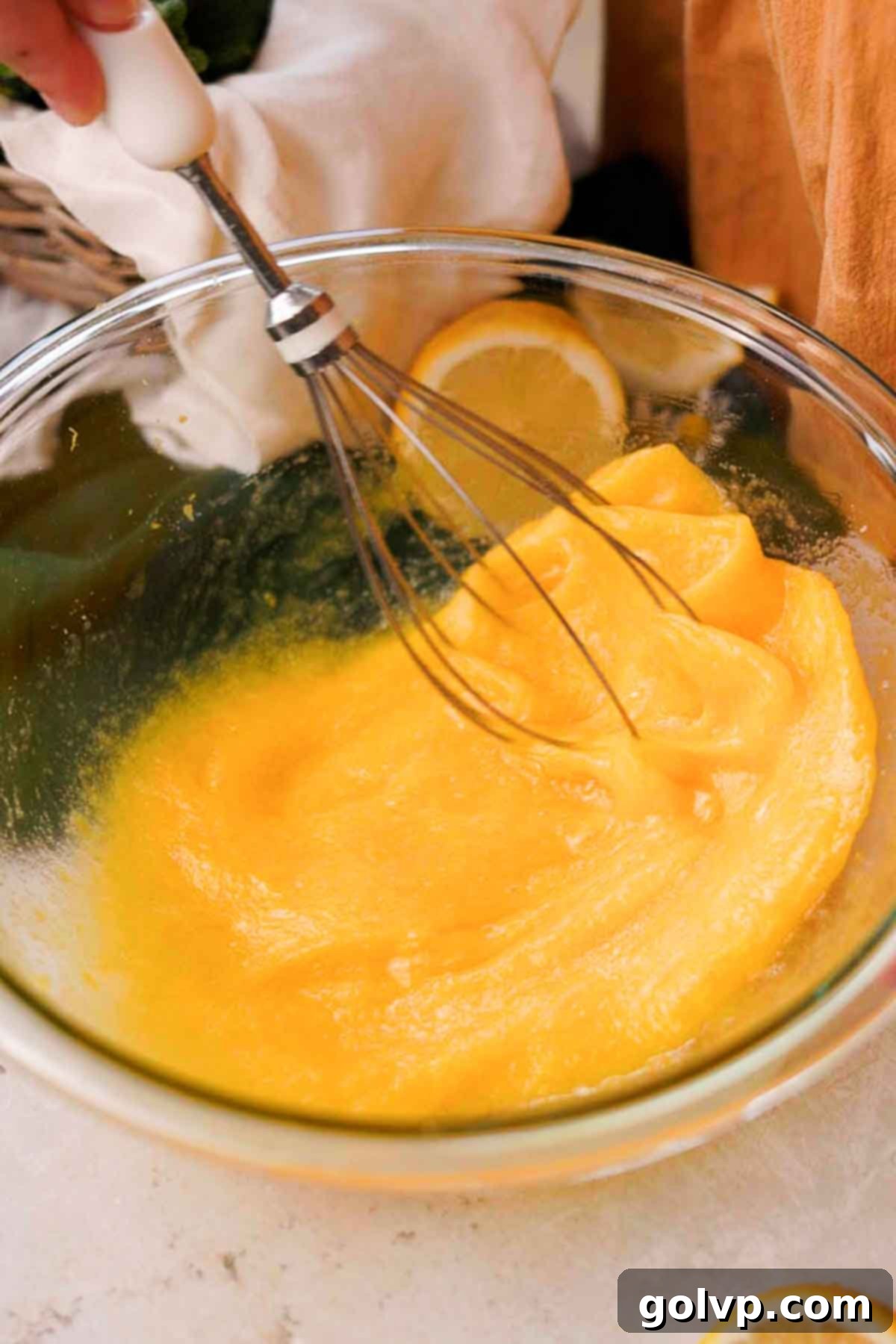 A wire whisk rapidly mixing three large eggs into the lemon-infused sugar mixture in a bowl, creating a smooth, pale batter.