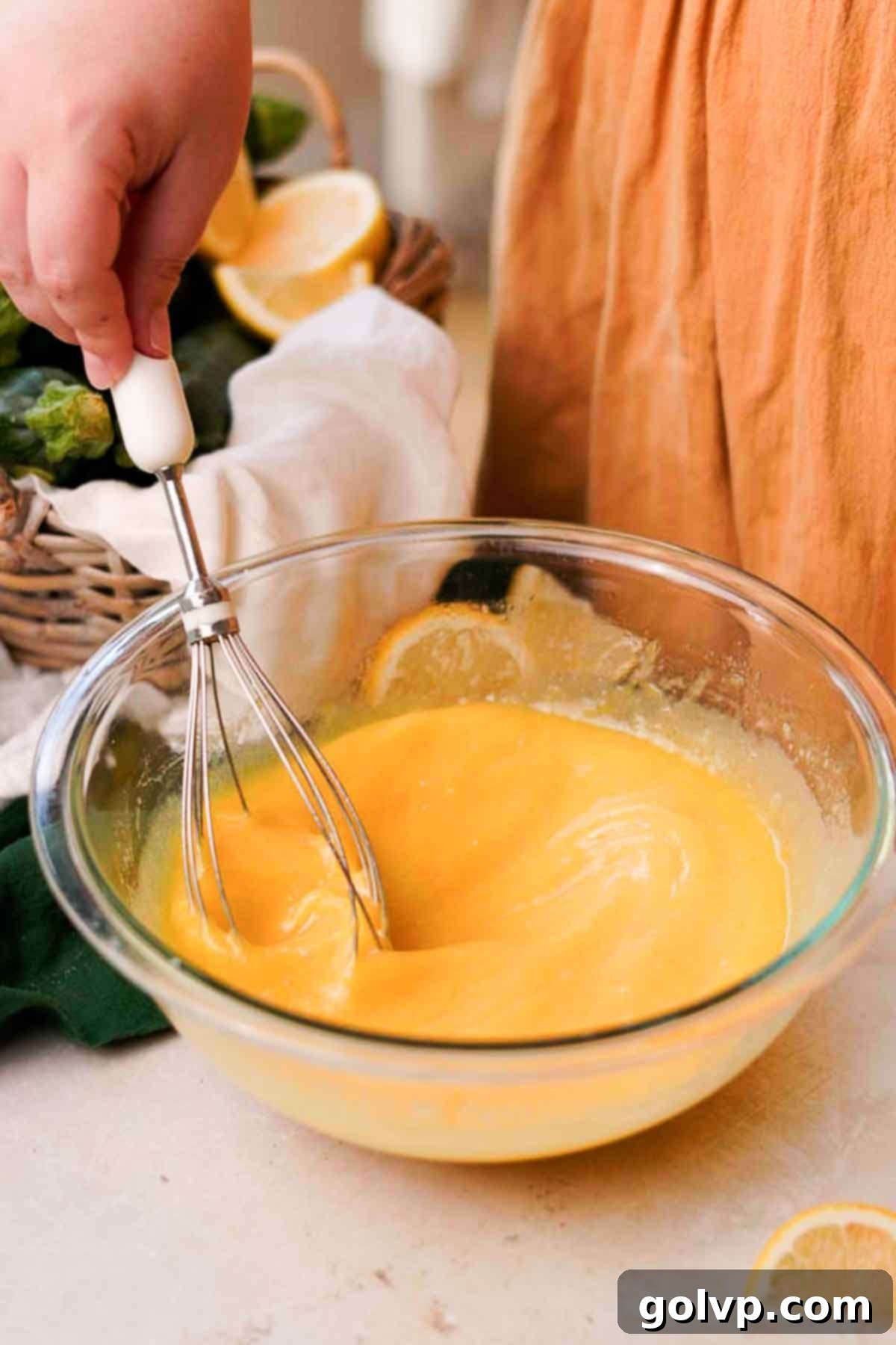 A hand whisking together the wet ingredients – melted butter, vanilla extract, and lemon juice – into the egg and sugar mixture until smooth.