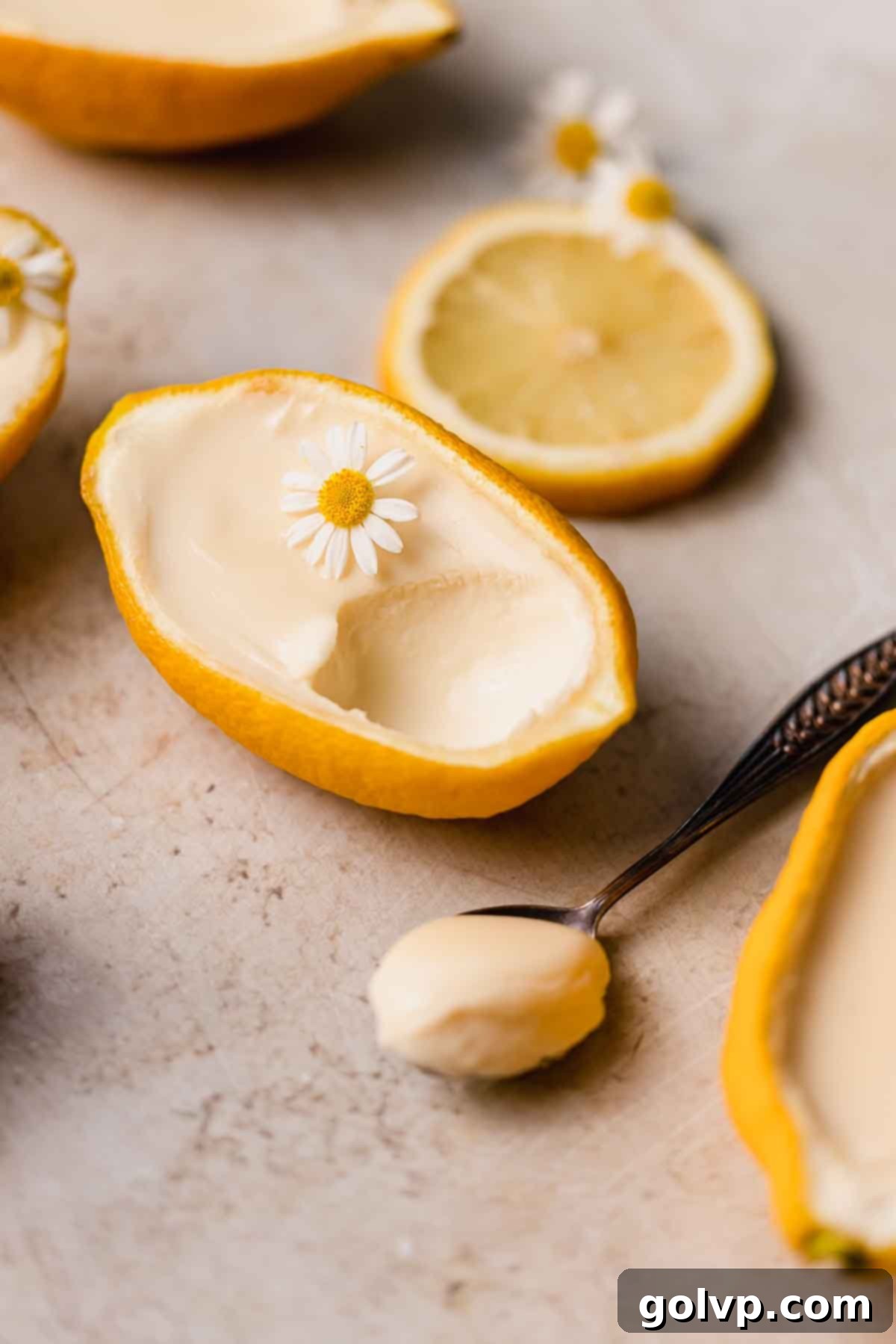 Delicate lemon posset served in a lemon rind, topped with a fresh chamomile flower, ready to be enjoyed.