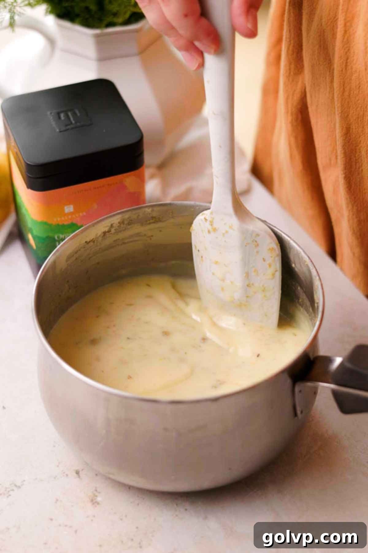 A spoon stirring the cooked lemon posset mixture in a saucepan, ensuring even heating and flavor distribution.