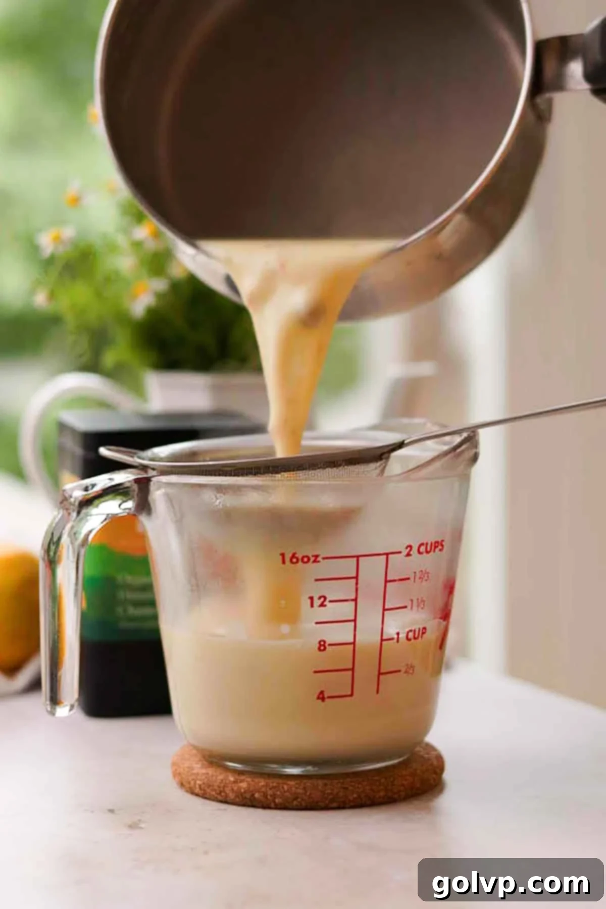 Straining the hot cream mixture through a metal mesh strainer to remove lemon zest and tea leaves, creating a smooth base.