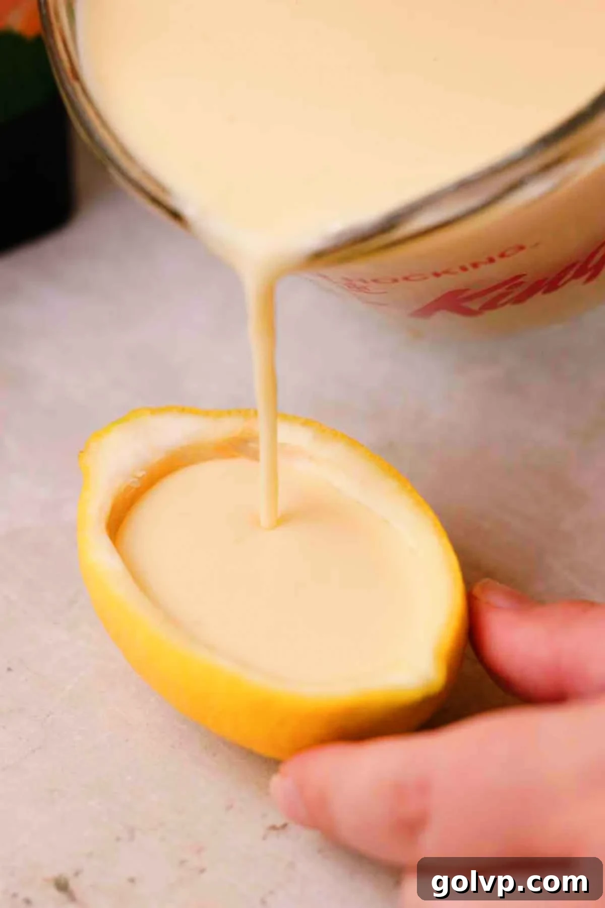 Pouring the creamy lemon posset mixture carefully into a hollowed-out lemon rind.