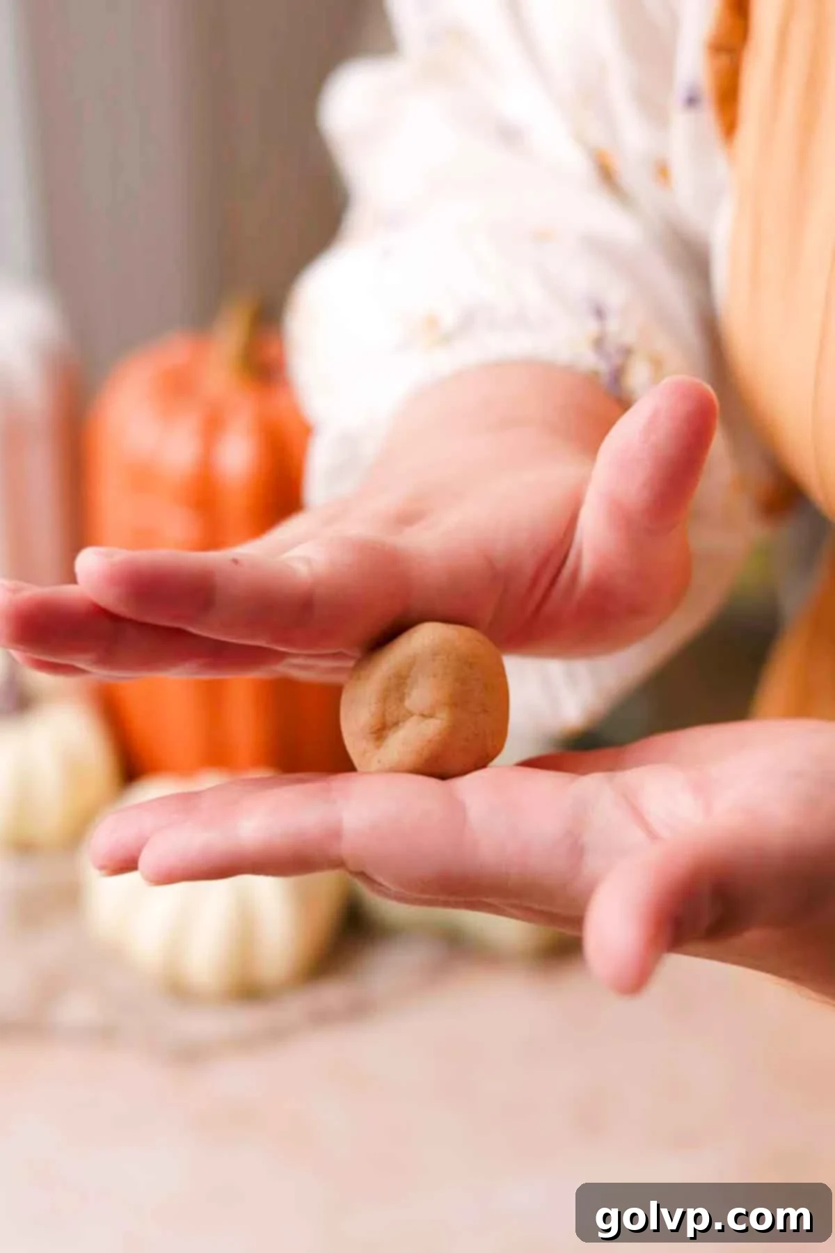Scooping cookie dough balls onto a parchment-lined baking sheet and creating thumbprint indents with raised walls.