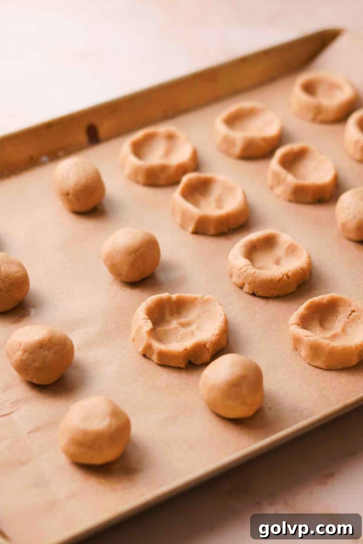 Chilled, shaped cookie dough with indents on a baking sheet, ready for filling.