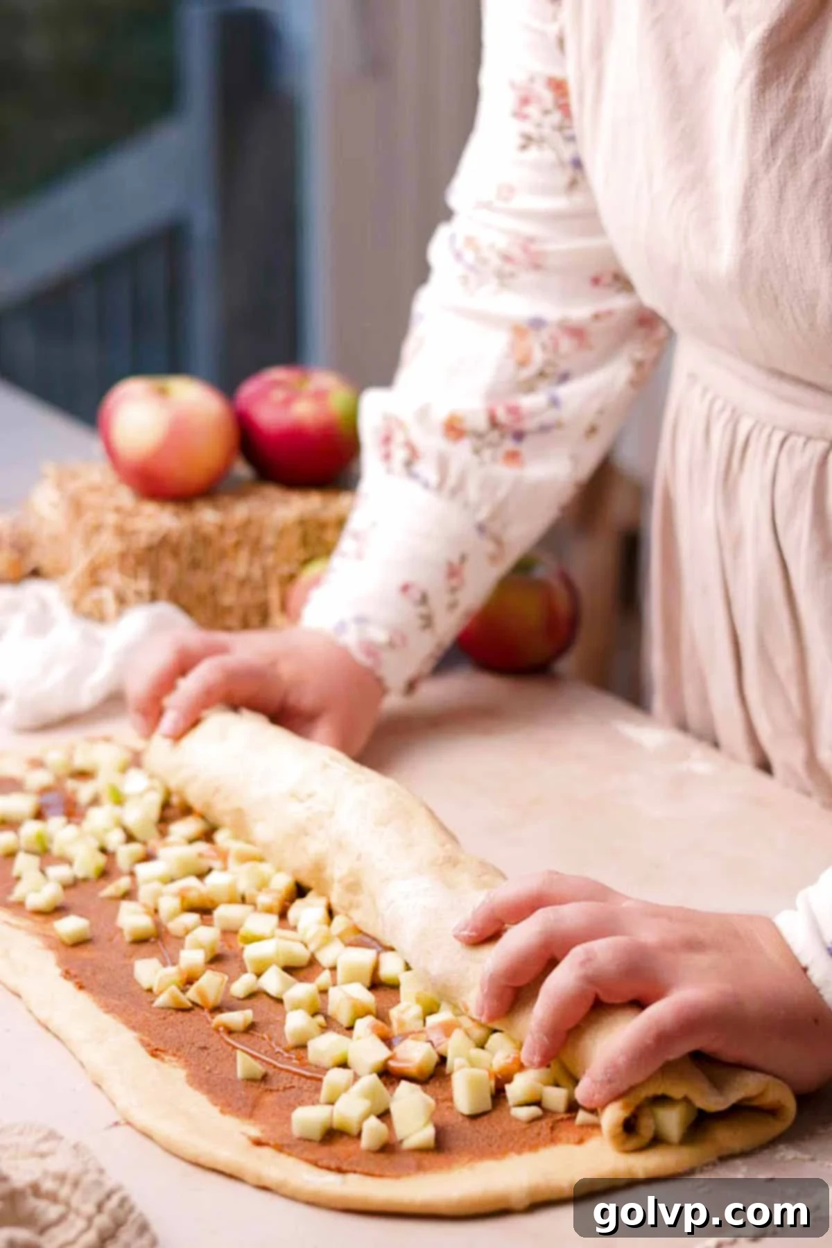 Gently rolling the dough, filled with spiced apples and cinnamon butter, into a tight log from the long edge.