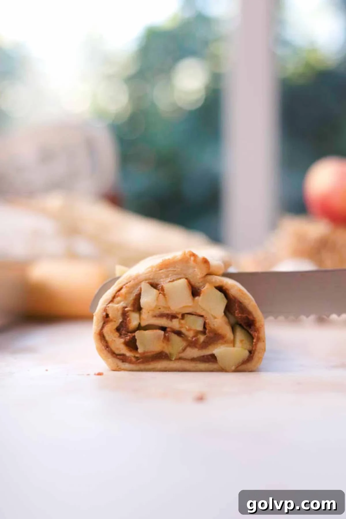 A log of apple cinnamon roll dough being cut into individual slices using dental floss for clean, even rolls.