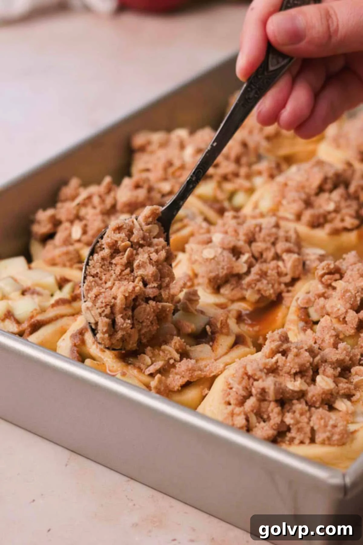 Sprinkling the cinnamon crumble mixture generously over the apple cinnamon rolls in the baking pan before baking.