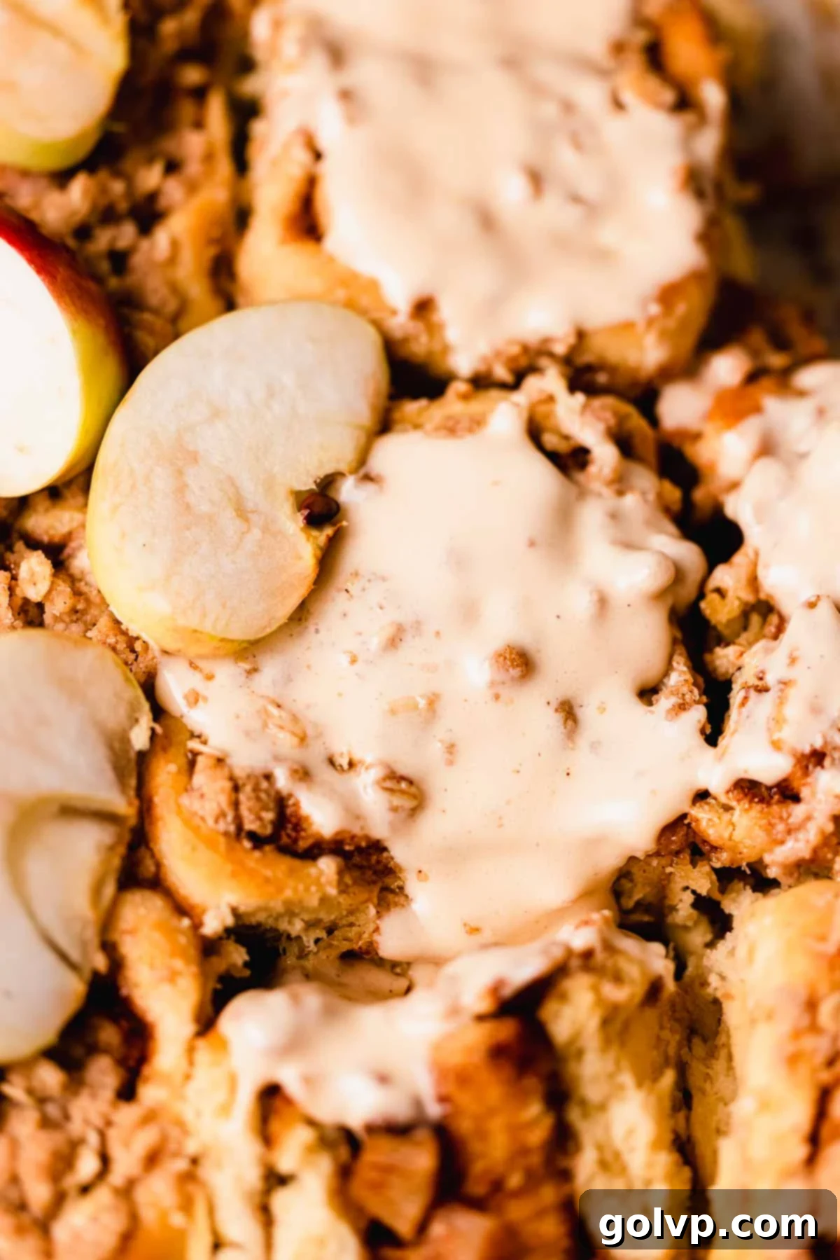 Close-up of a glazed apple cinnamon roll with fresh apple slices and a hint of crumble on top.