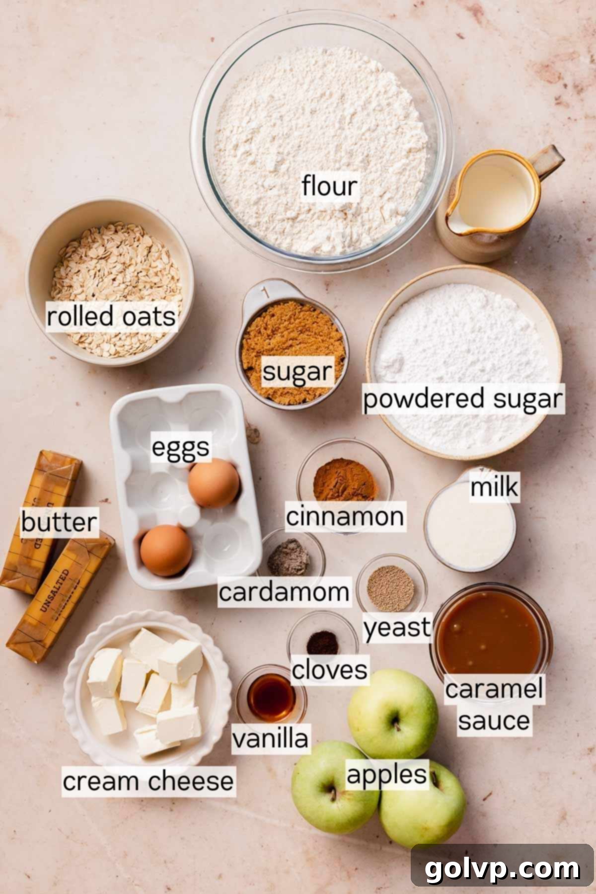 Arrangement of fresh apples, butter, spices, flour, and other ingredients laid out for making caramel apple cinnamon rolls.