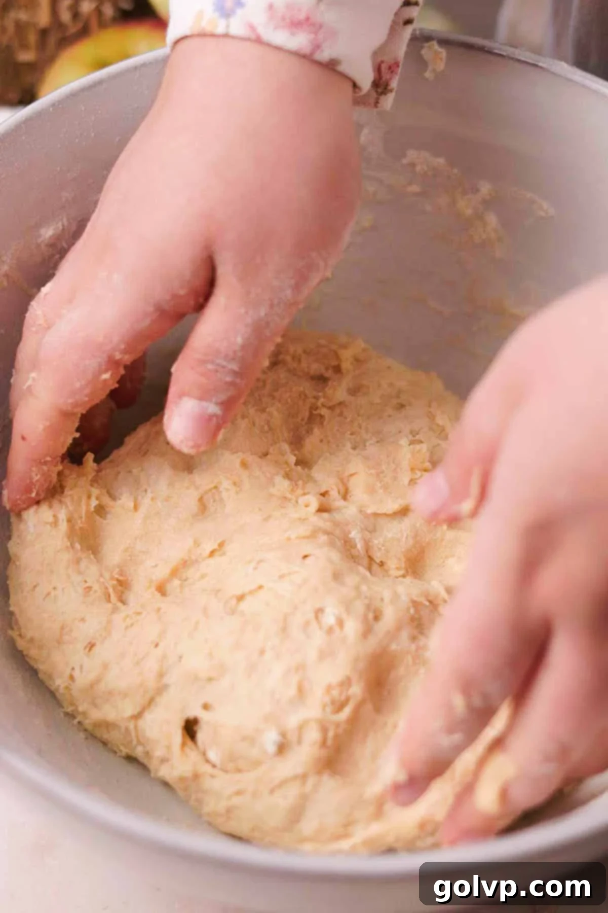 Mixing the wet and dry ingredients by hand to form a sticky, shaggy apple cinnamon roll dough in a large bowl.