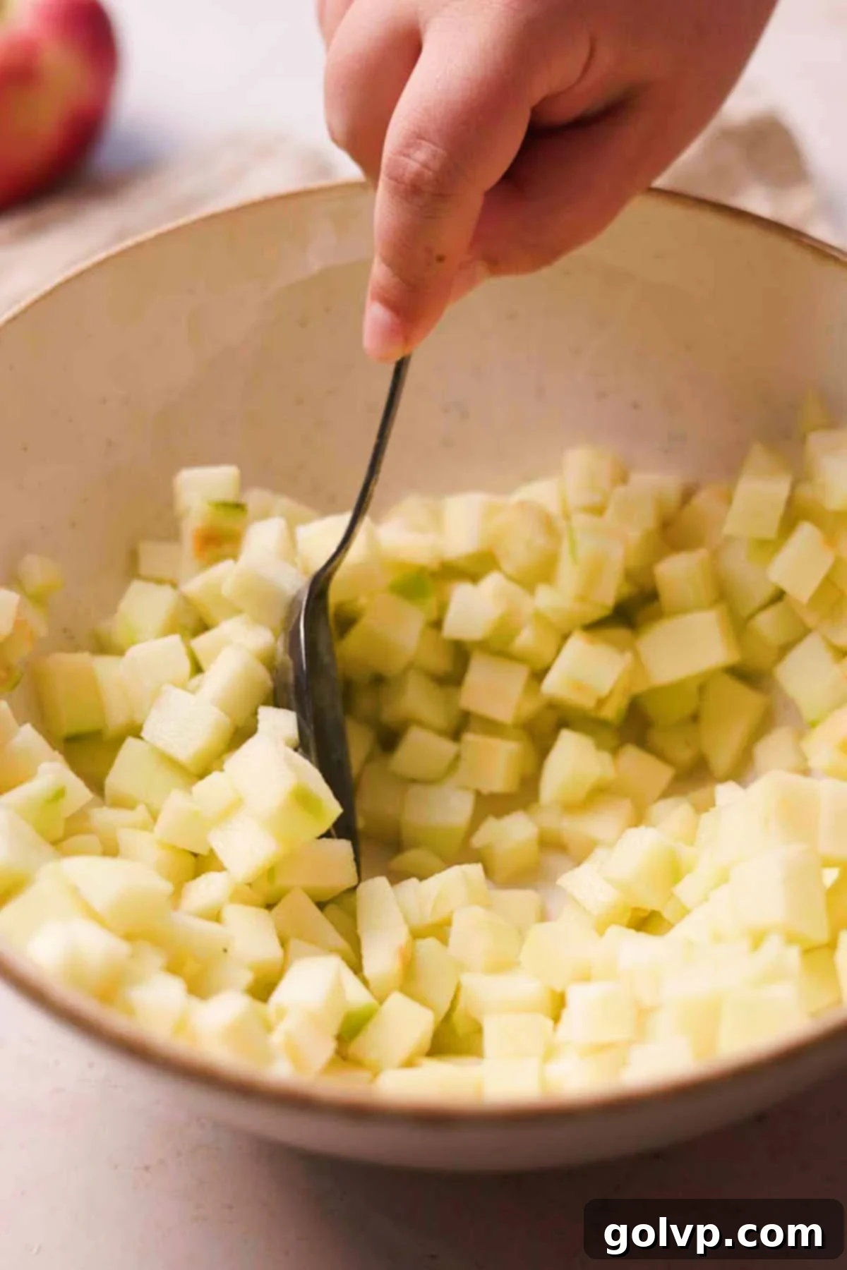 Diced apples being tossed with fresh lemon juice in a bowl to prevent browning for the cinnamon roll filling.