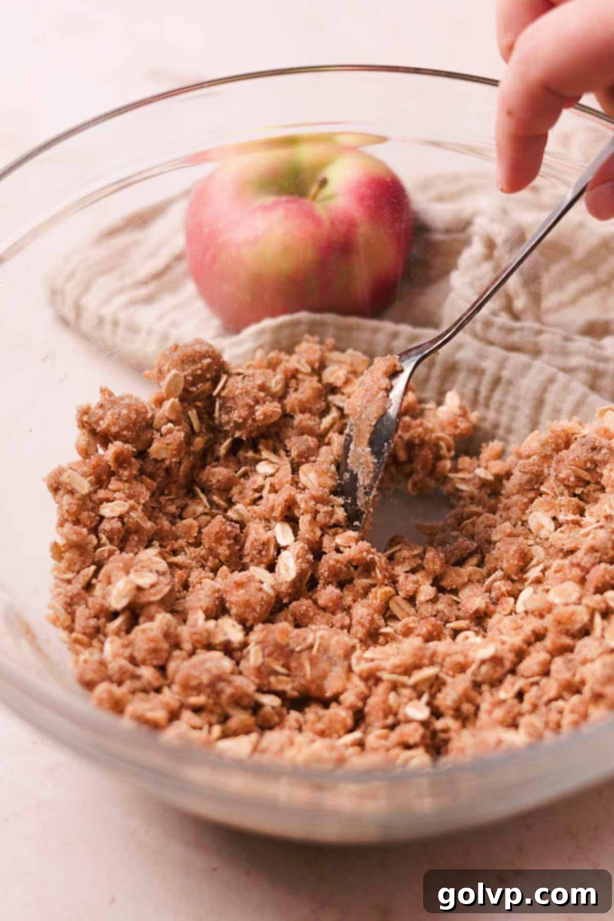 Mixing brown sugar, granulated sugar, cinnamon, oats, flour, and melted butter together in a glass bowl to create a crumbly topping.