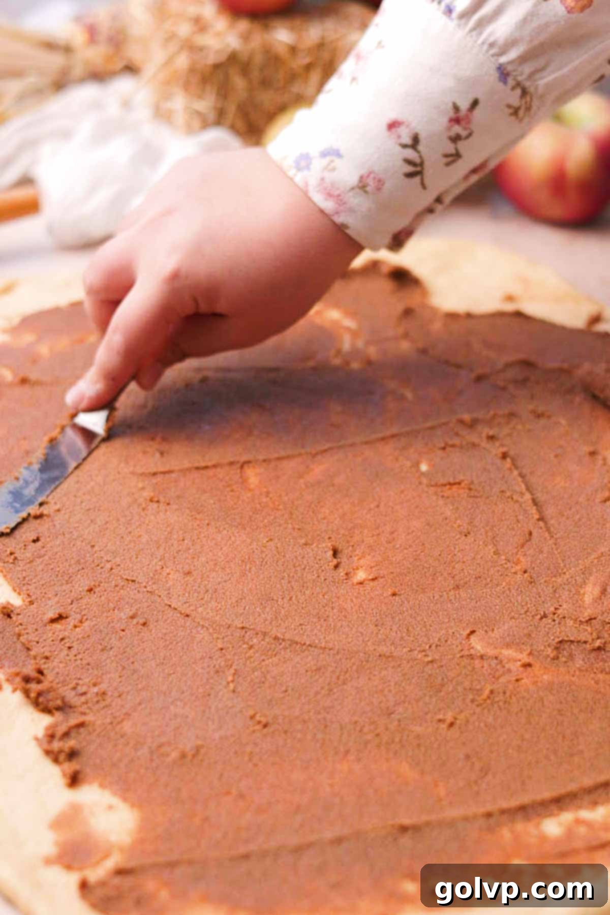 Spreading a thick layer of cinnamon butter sugar filling evenly onto a large rectangle of risen dough for the apple cinnamon rolls.