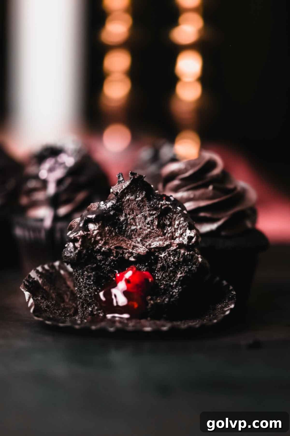 black velvet cupcake unwrapped with bite taken out zoomed out, showcasing the dark crumb and cherry filling