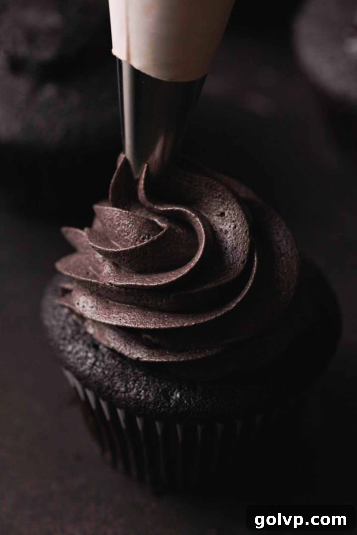 piping black cream cheese frosting onto a black velvet cupcake