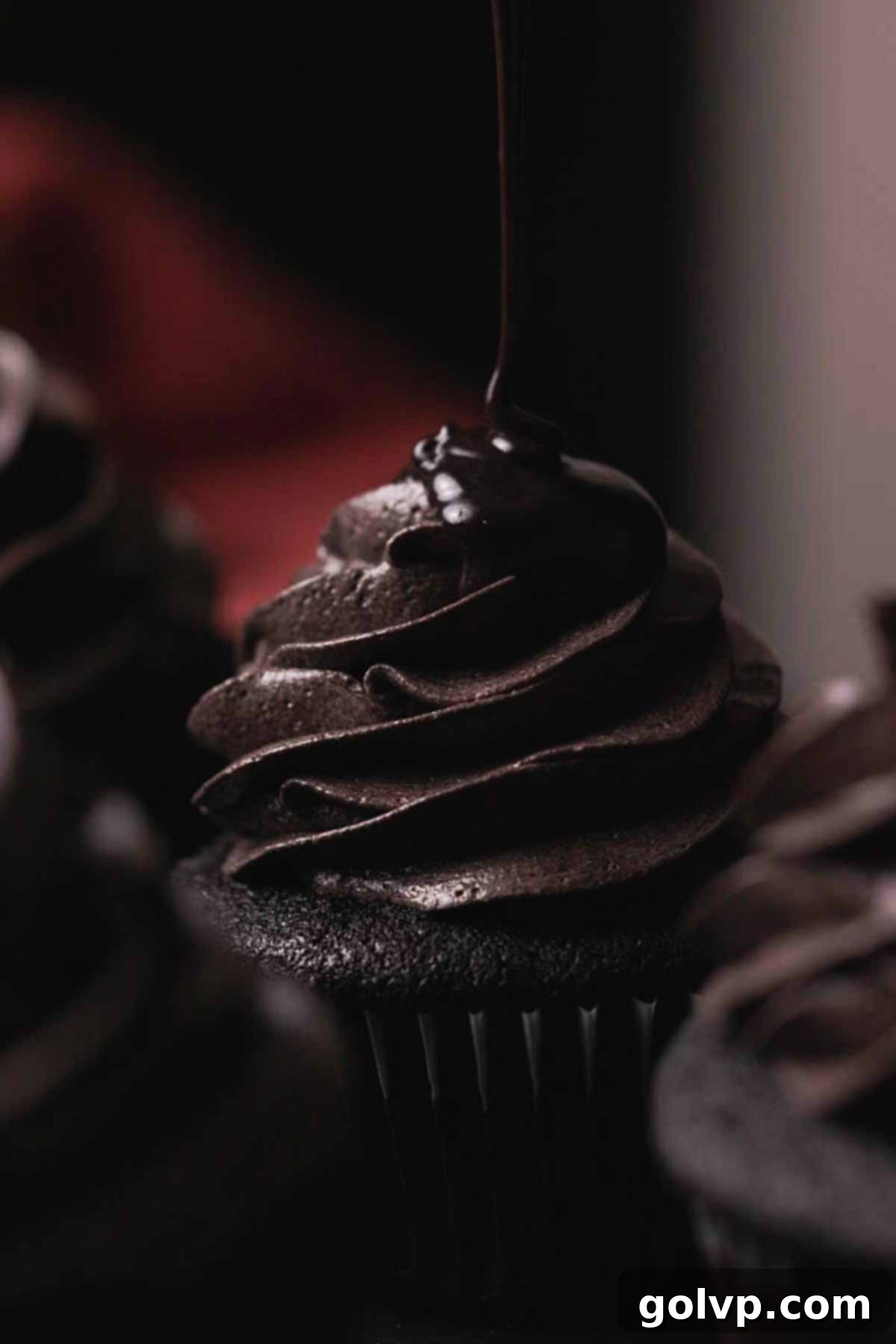 drizzling black chocolate drip onto a frosted black velvet cupcake