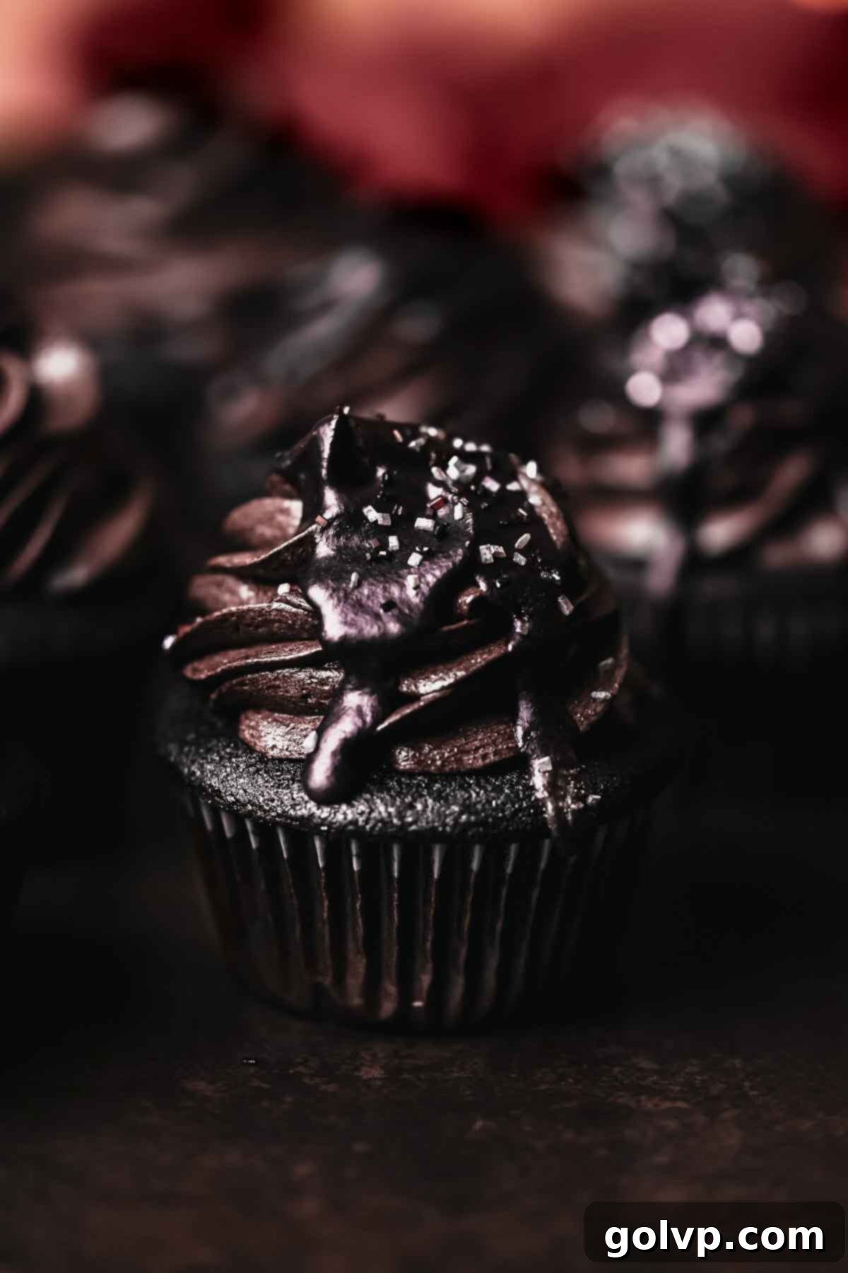closeup of black velvet cupcake with dark frosting and cherry peeking out