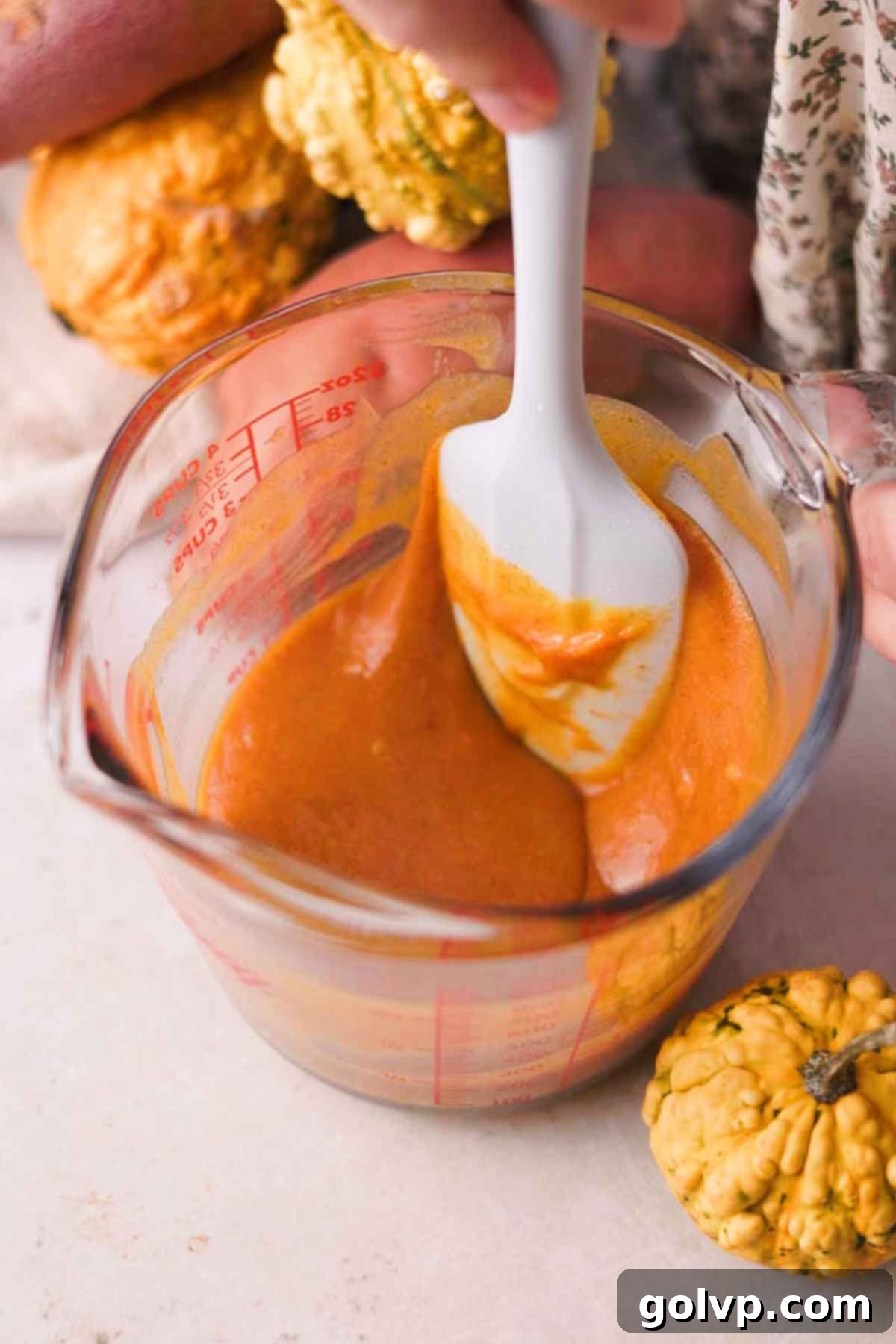 A pitcher containing egg yolks, sugar, and sweet potato puree being stirred until smooth.