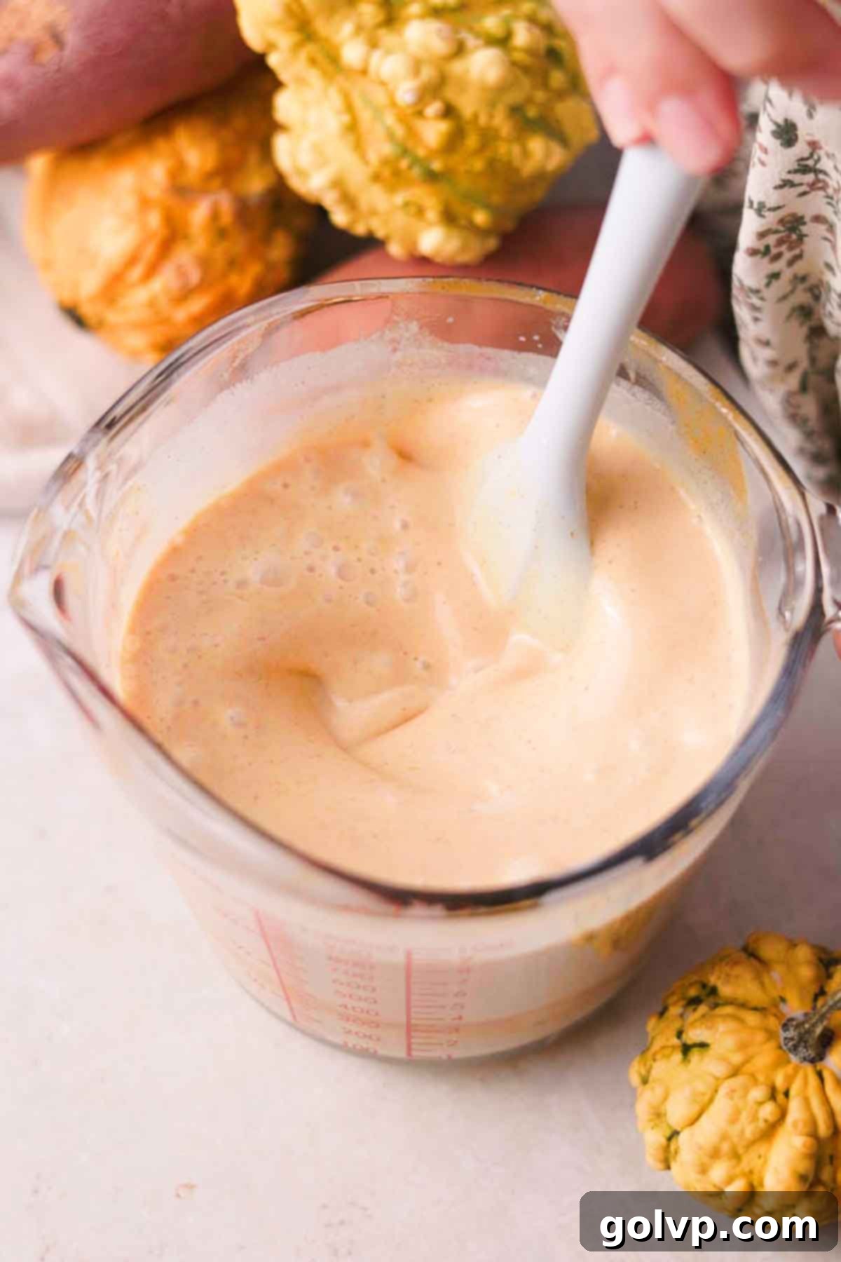 A hand stirring the crème brûlée mixture, which now includes cream, milk, and spices, in a measuring cup.