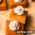 Close-up of a perfectly portioned pumpkin pie bar, highlighting its creamy filling and golden-brown brown butter shortbread crust, topped with a swirl of whipped cream.