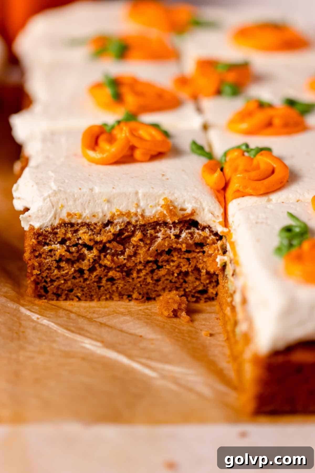 A festive pumpkin cake on parchment paper, beautifully frosted with white cream cheese frosting and adorned with cheerful orange piped pumpkins, creating a perfect autumnal display.