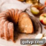 A beautifully sliced apple cider bundt cake resting on a cake plate, showcasing its moist texture and inviting cinnamon-sugar coating.