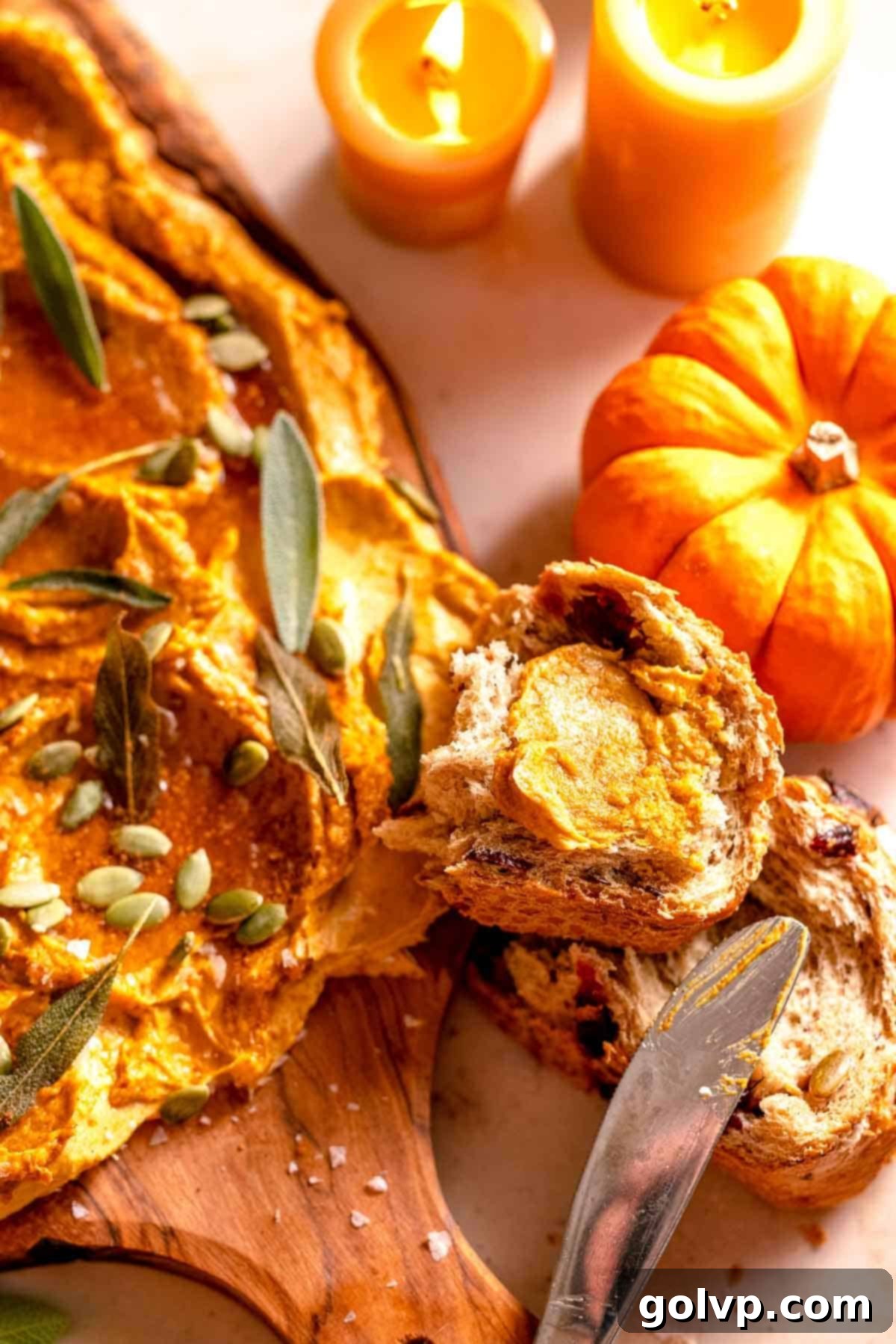 Creamy pumpkin butter spread on a slice of cranberry seeded bread, surrounded by decorative mini pumpkins and lit candles, creating a warm, inviting fall scene.