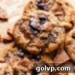 A delicious brown butter toffee chocolate chip cookie resting on a baking sheet, golden brown and speckled with melted chocolate and toffee bits.
