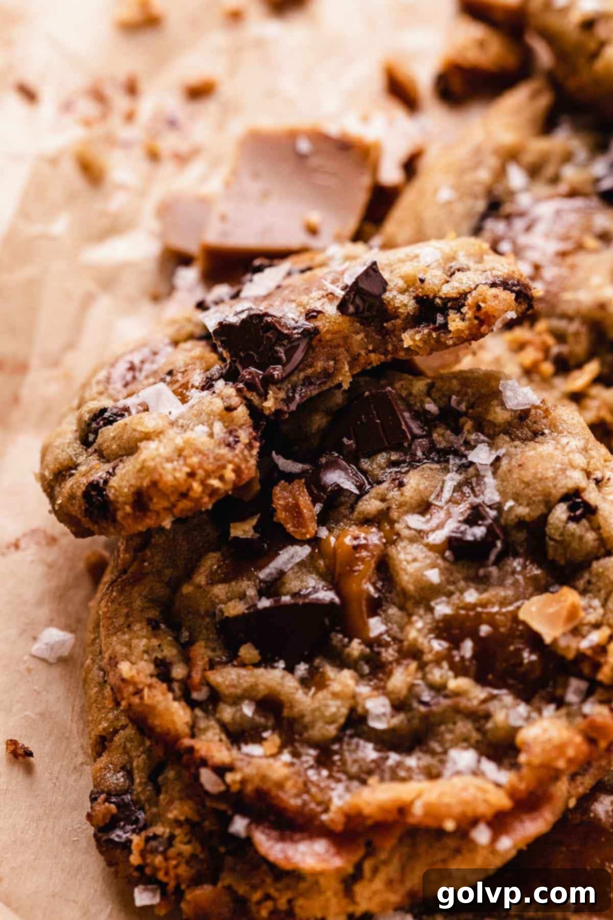 A partially bitten brown butter toffee chocolate chip cookie stacked on a whole one, showing its soft, gooey interior and melted toffee puddles.