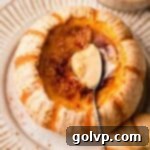 A delicate spoon poised within a pumpkin crème brûlée, served inside a charming mini orange and white pumpkin, ready to be enjoyed.