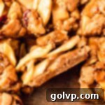 Close-up of a salted caramel apple pie bar on a square of parchment paper, showing its crumb topping, gooey apple filling, and golden-brown crust.