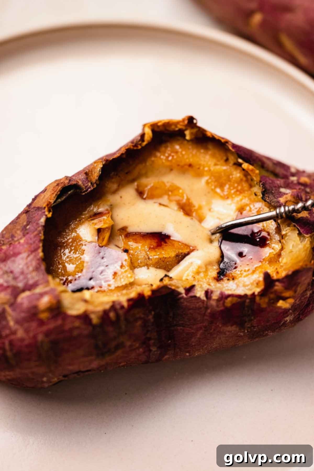 Close-up of a spoon breaking through the shimmering, golden-brown caramelized topping of a sweet potato crème brûlée, highlighting its glossy finish and inviting texture.