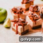 Close-up of a perfectly cut caramel apple cheesecake bar, showcasing its distinct graham cracker crust, creamy filling, and generous spiced apple topping.