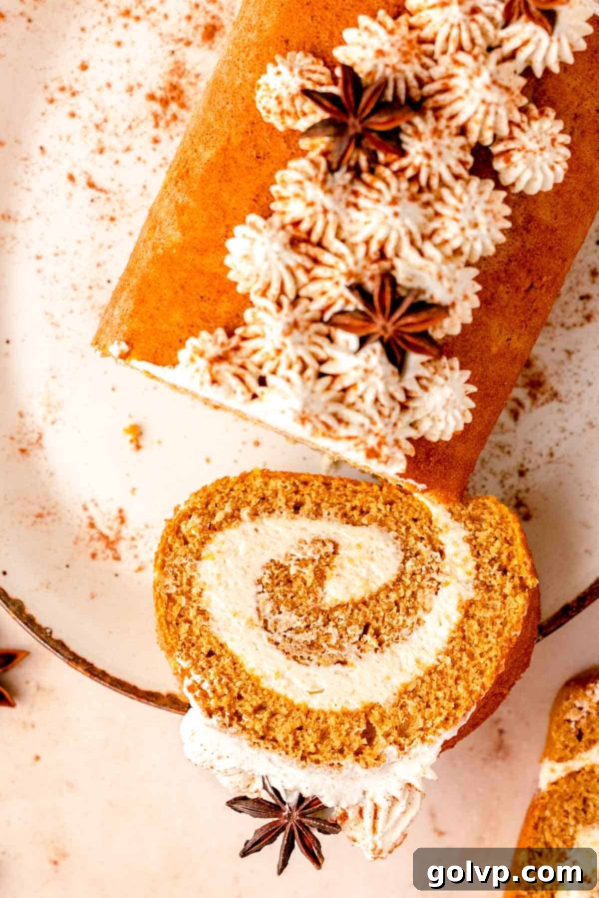 Several slices of pumpkin cheesecake roll arranged on a plate, each topped with delicate piped whipped cream stars, ready for an elegant presentation.