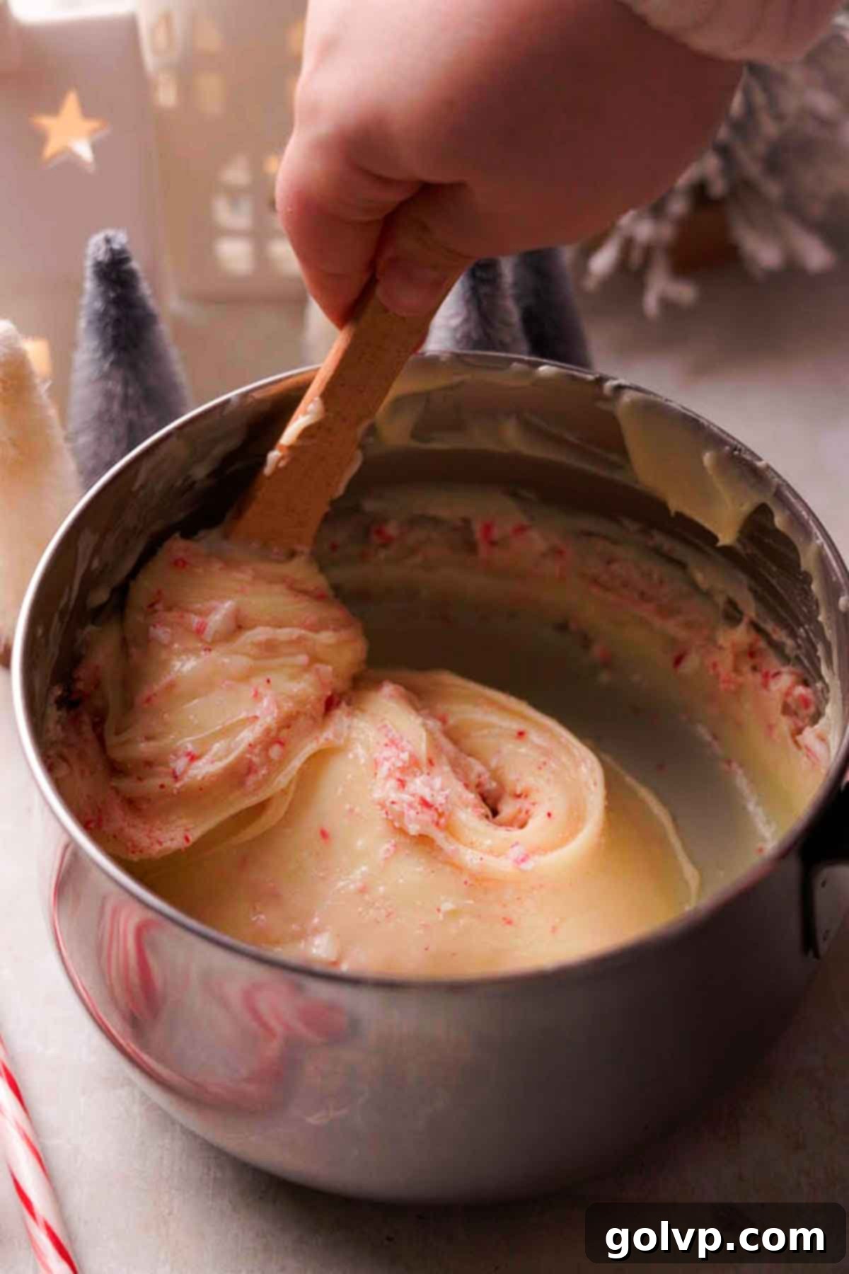 Indulgent Peppermint Fudge 6 A spoon stirring crushed peppermint candies into a bowl of melted white chocolate peppermint fudge mixture.