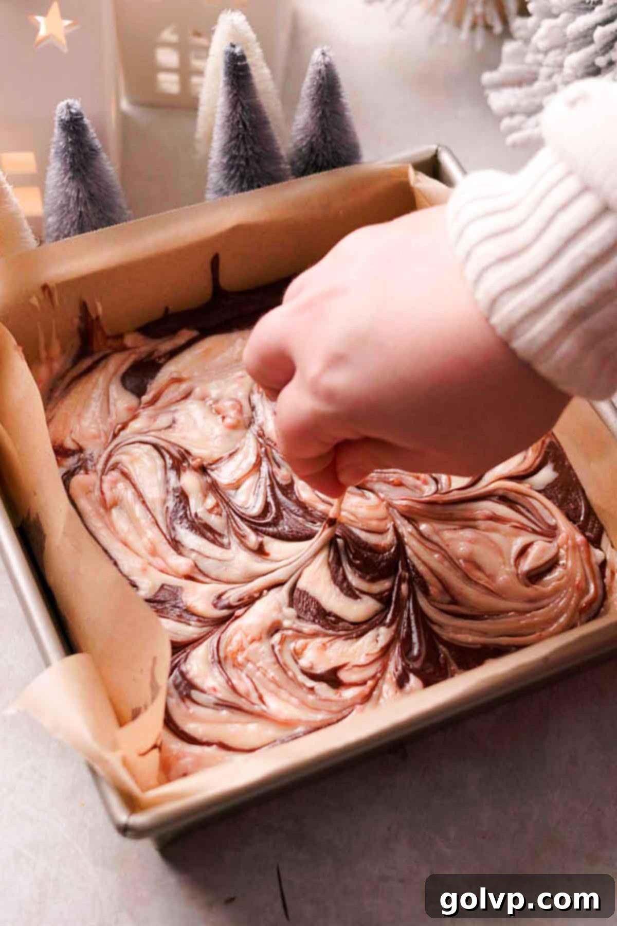 Indulgent Peppermint Fudge 8 A hand gently swirling the two colors of peppermint fudge together in the pan with a toothpick to create a marble effect.