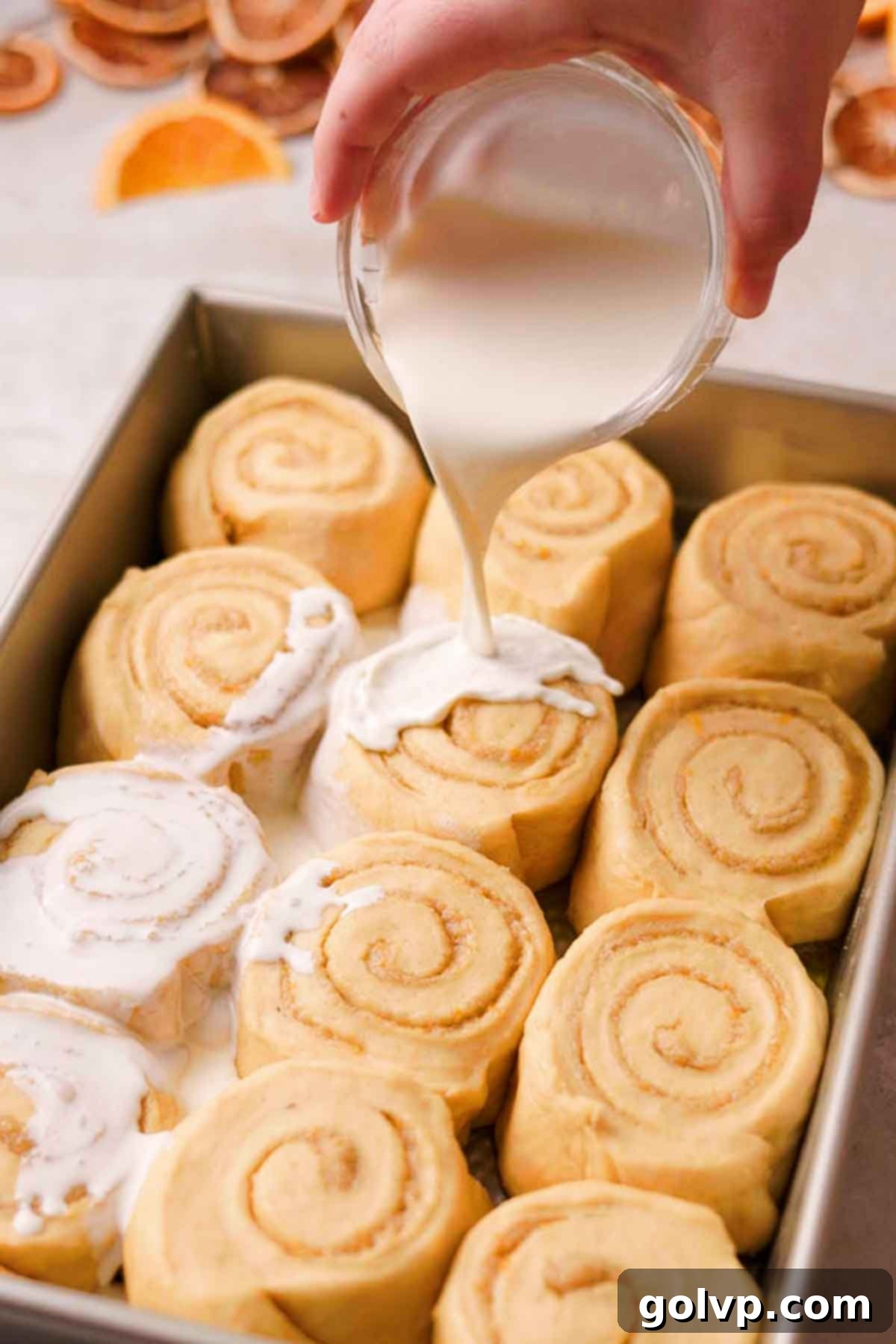 pouring cream over risen orange cinnamon rolls